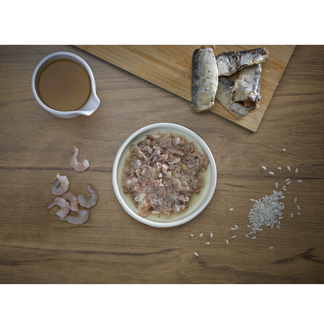 Some fresh ingredients, sardine, shrimp, broth and rice. In the middle of these, there is a bowl of Fish 4 Cats Sardine & Shrimp served in a bowl.