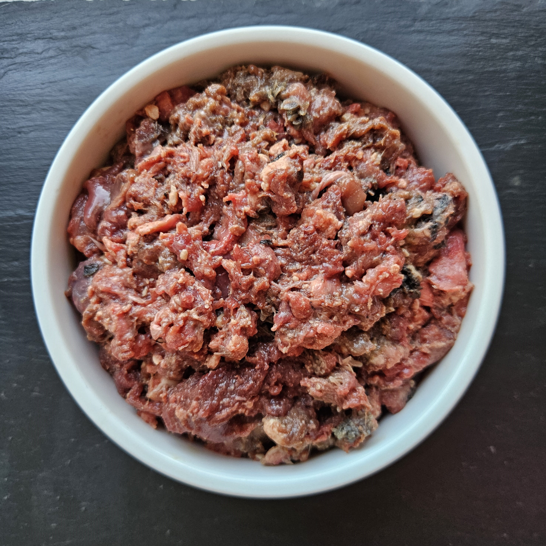 Barkin Bistro 80/10/10 Raw Beef Dog Food. It is in a white bowl. You can see the different textures.