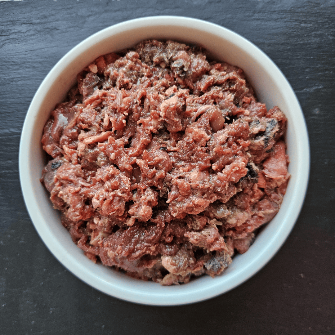 Barkin Bistro 80/10/10 Raw Beef Dog Food. It is in a white bowl. You can see the different textures.