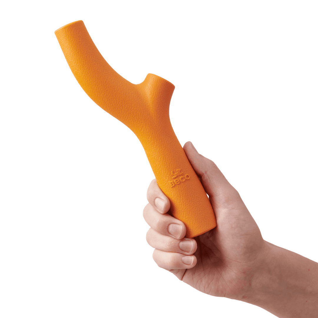 Hand holding a Beco Rubber Orange Stick dog toy.