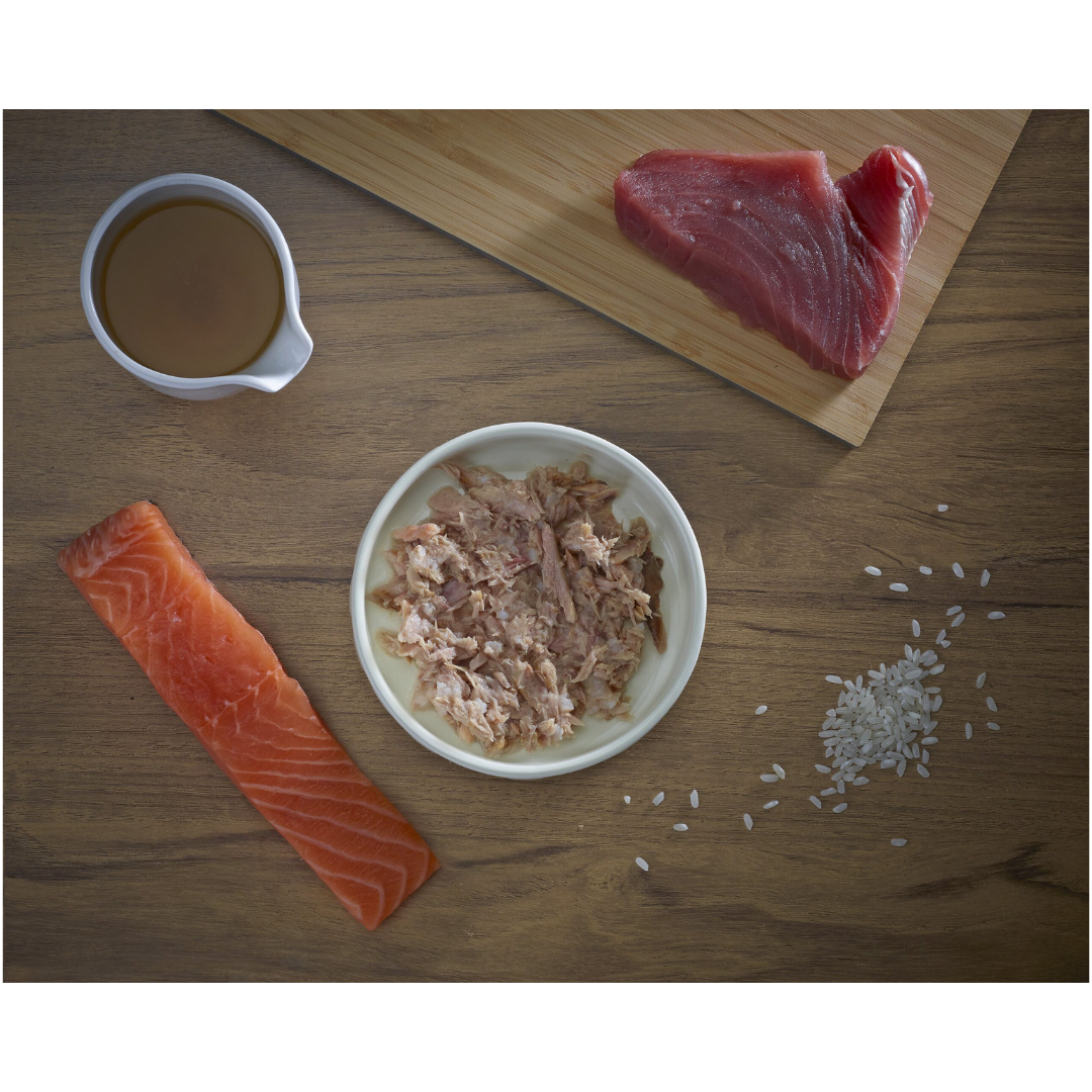 Some fresh ingredients, tuna, salmon, broth and rice. In the middle of these, there is a bowl of Fish 4 Cats Tuna & Salmon served in a bowl.