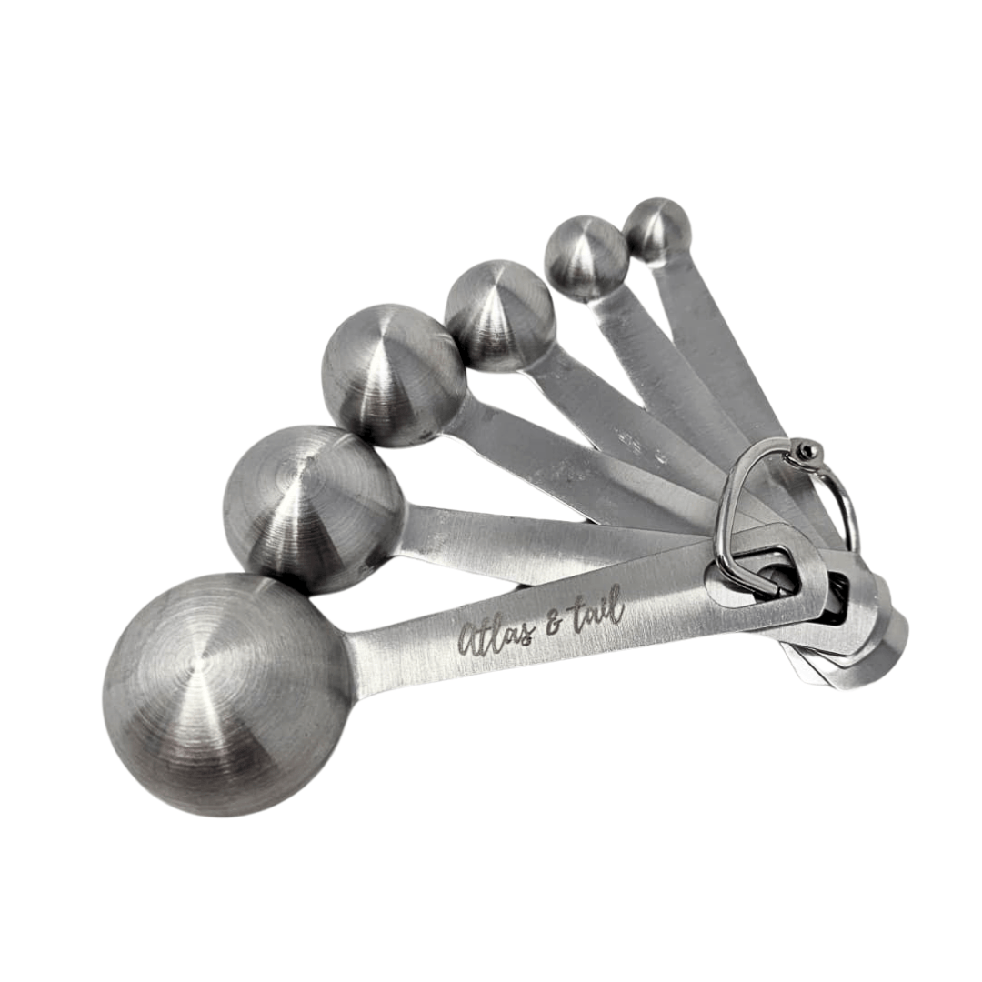 Set of silver measuring spoons with 'Atlas & Tail' branding on a white background