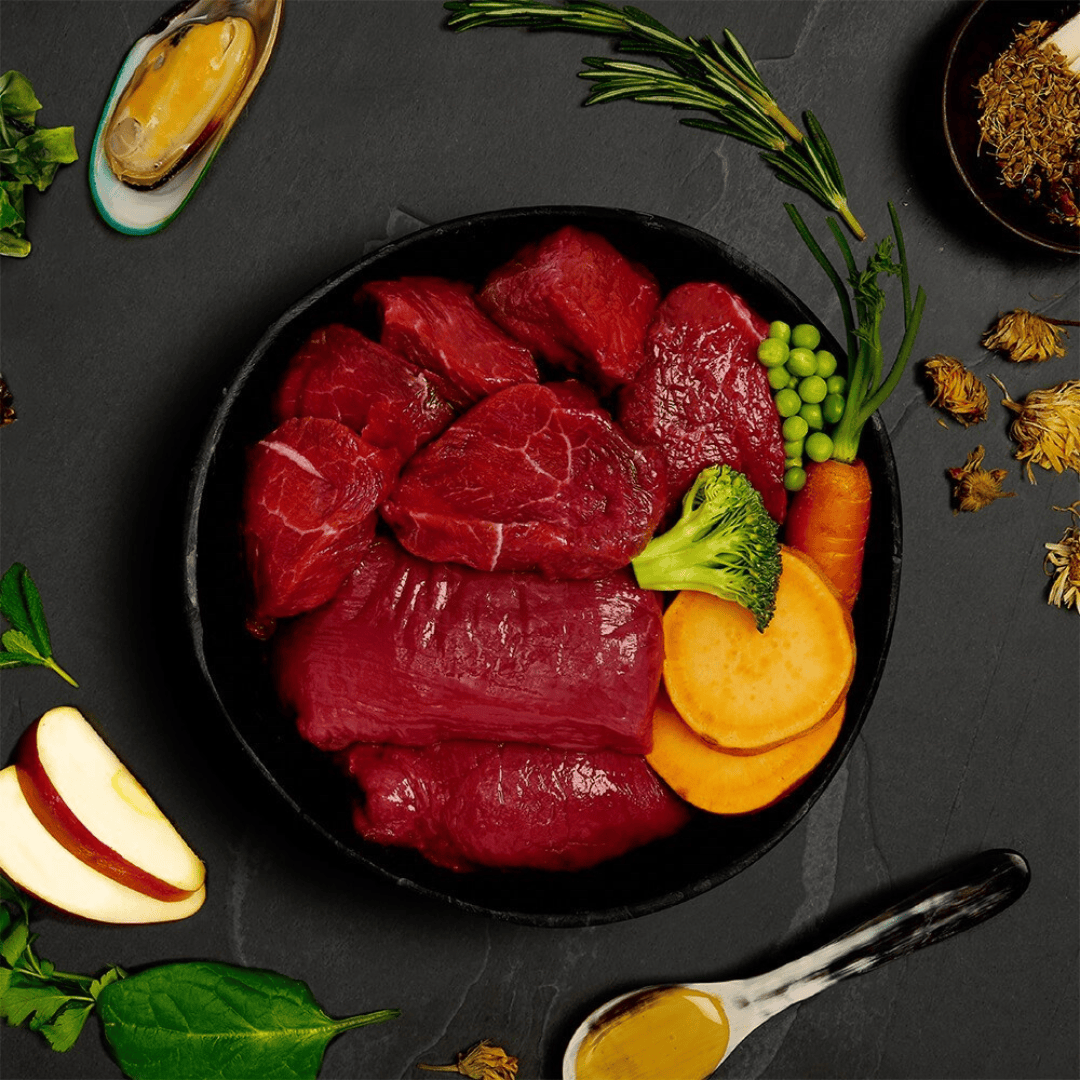 The fresh ingredients of the Canagan Venison and Wild Boar Stew Wet Food 400g in a bowl. There are other functional additions placed around the bowl including green lipped mussels.