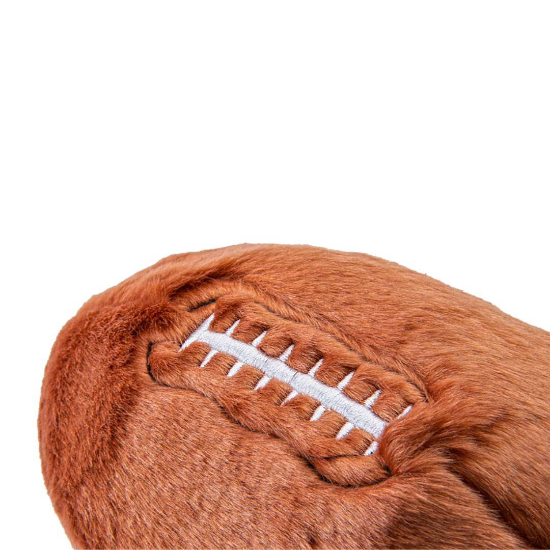 A close up of the Fluff & Tuff Football Plush Dog Toy against a white background. It is brown in colour and white stitching to mimic that of a football.