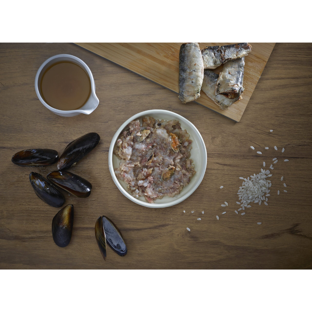 Some fresh ingredients,sardine, mussel, broth and rice. In the middle of these, there is a bowl of Fish 4 Cats Tuna & Salmon served in a bowl.