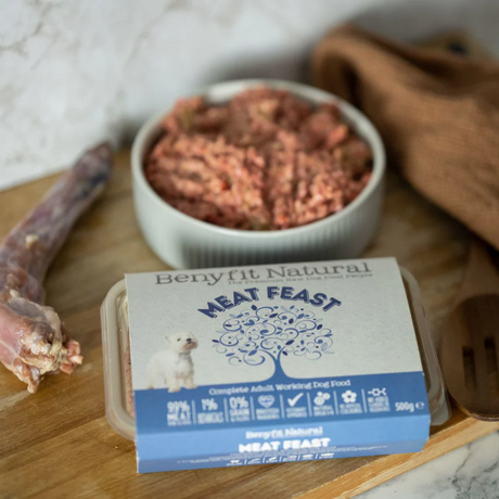 Bowl of and pack of Benyfit Natural Meat Feast raw dog food, to the right of a raw turkey neck.
