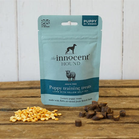 Bag of Innocent Hound Puppy Training Treats on wooden boards with yellow split peas and loose puppy treats in the foreground.