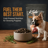 Kudo puppy food packaging with a bowl of cold pressed dog food and a puppy on a wooden surface.