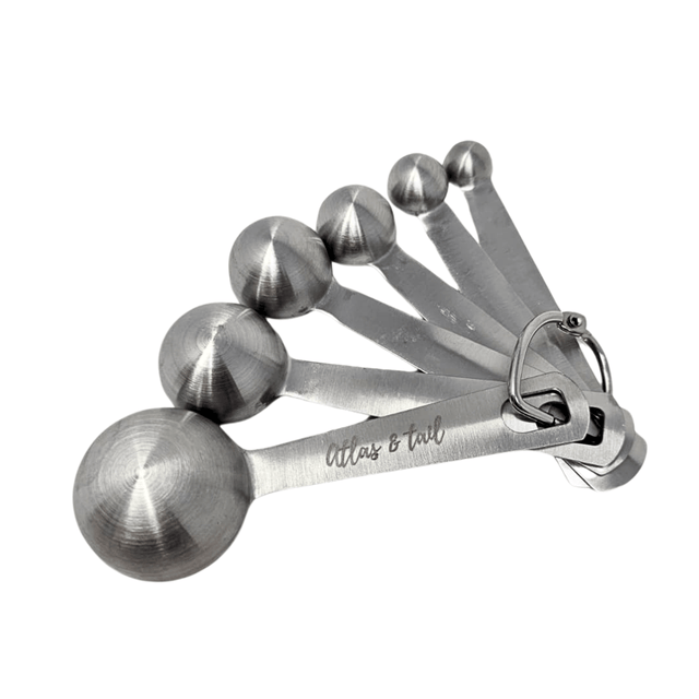 Set of silver measuring spoons with 'Atlas & Tail' branding on a white background