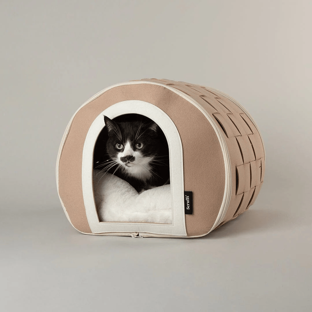 Cat peeking out from a beige Stockholm Cat Cave pet bed with a white interior on a neutral background