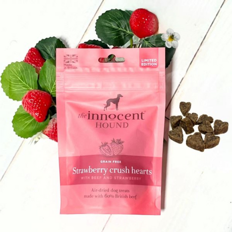 Bag of Innocent Hound Strawberry Crush Hearts laying on a bunch of strawberries, with loose treats beside them.