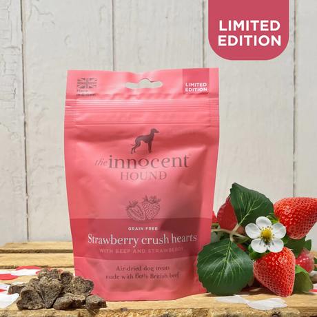 Bag of Innocent Hound Strawberry Crush Hearts beside a pile of the loose treats and a bunch of strawberries.